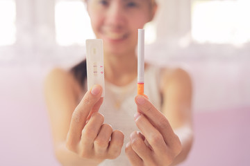 Pregnant asia woman in white dress hole a cigarette and pregnancy test strip for choice for health, close up of pregnancy test strip