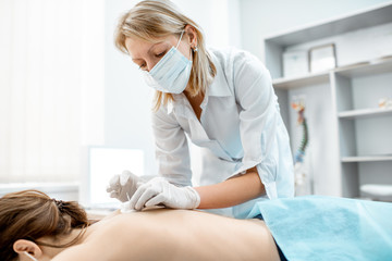 Neuropathologist puts needles into the woman's back removing inflammation of the muscles during the acupuncture treatment in the office