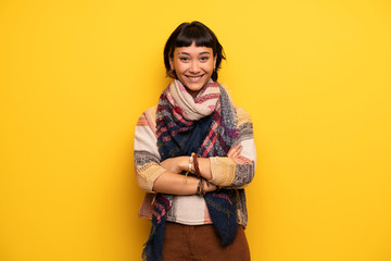 Young hippie woman over yellow wall keeping the arms crossed in frontal position