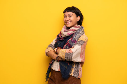 Young hippie woman over yellow wall keeping the arms crossed while smiling