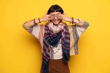 Young hippie woman over yellow wall covering eyes by hands. Surprised to see what is ahead