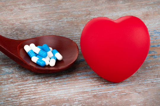 medicine pills, tablets and capsules on wooden spoon with heart