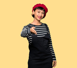 Young woman with beret shaking hands for closing a good deal over yellow background