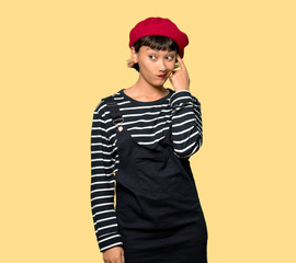 Young woman with beret making the gesture of madness putting finger on the head over yellow background