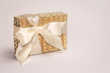 Beautiful shiny golden present box with a silk bow on pastel background. Copy space.
