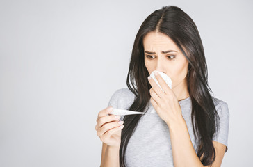 Portrait of a pretty woman having flu. Girl blowing nose standing isolated over white background.