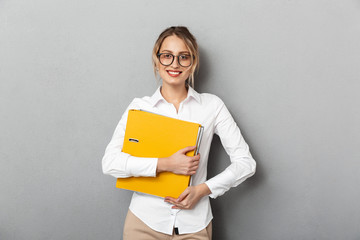 Photo of happy businesswoman wearing glasses holding paper folders in the office, isolated over...