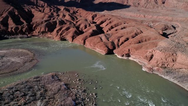 Aerial view of red eroded terrain next to the Colorado River tilting up to look at the desert red cliffs in Moab Utah.