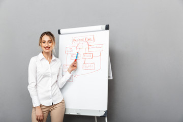 Image of smiling businesswoman in formal wear standing and making presentation using flipchart in the office, isolated over gray background - obrazy, fototapety, plakaty