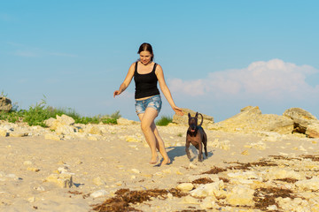 Young beauYoung girl walking (play) with her dog xoloitzcuintli on sand beach at sunsettiful girl playing with a dog on a sandy beach at sunset