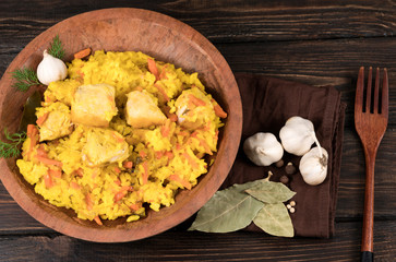 Pilaf with vegetables and chicken in a wooden bowl on a wooden background