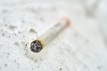 Half-smoked cigarette lying on the snow macro photo