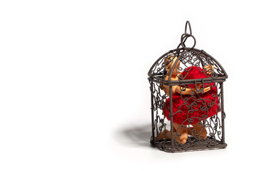 Action figure sitting in cage and holding red heart on white background. Concept of Love and imprisonment