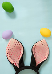 Top view Bunny ears headband and colorful painted eggs over blue background