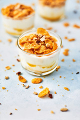 Healthy breakfast or dessert. Tasty corn flakes with yogurt, almond and honey in a small glass on light blue background. Copy space for text.