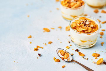 Healthy breakfast or dessert. Tasty corn flakes with yogurt, almond and honey in a small glass on light blue background. Copy space for text.