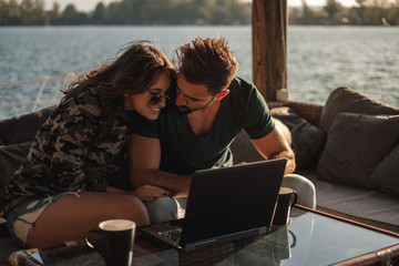 Couple smiling and working on laptop bu the river