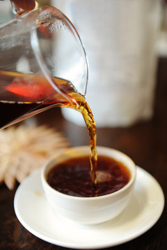 Pour freshly brewed black tea from a glass jug into a ceramic tea bowl