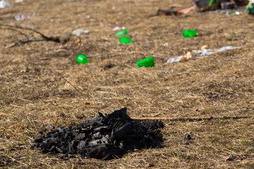Fototapeta na wymiar Close-up coals from campfire on spring grass in mountains left by tourists on background of scattered garbage and plastic cups. Environmental pollution.