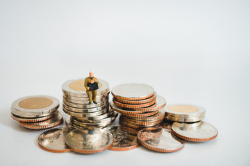 Miniature people, man waiting on pile of coins on white background using as business and financial concept