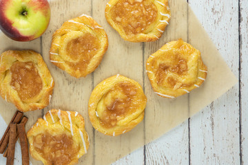 apple danish on parchment paper with apple and cinnamon sticks from above on white wood rustic background