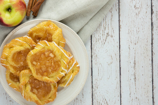 apple danish with linen napkin apple and cinnamon sticks on a plate and rustic white wood background