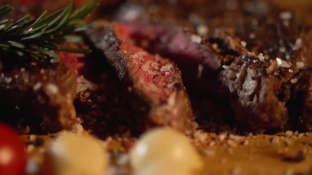 Salt sprinkled on delicious sliced roasted meat lying next to red tomatoes and onions on a cutting board close-up.