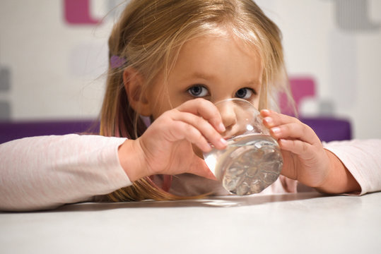 Little girl drinks water from a glass at the table