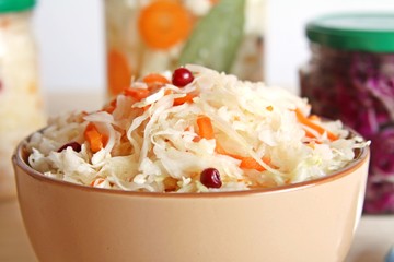 Fermented vegetables cabbage with carrot and cranberry in bowl with cauliflower and red cabbage in glass jar background