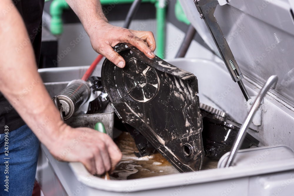 Wall mural Mechanic degreasing a car engine part at service repair station .