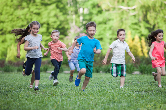 A group of happy children of boys and girls run in the Park on the grass on a Sunny summer day . The concept of ethnic friendship, peace, kindness, childhood.