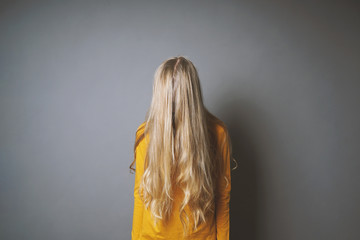 depressed young woman hiding her face behind long blond hair - shy or indifferent teenage girl