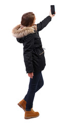 Back view woman in winter jacket who makes selfie with a smartphone. © ghoststone