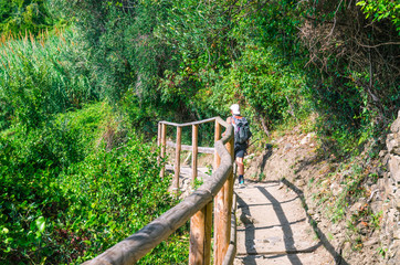 Tourist woman is hiking down pedestrian stone path trail with railing between Corniglia and...