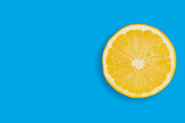 One circle slice of fresh ripe orange with pulp and peel on blue table on kitchen with copy space for your text. Top view. Concept of prepare of vegetarian food