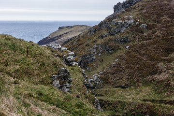 rocky mountain slopes overgrown with green grass and brown plants, moss, in the middle of the valley, which goes to the sea, visible behind the mountains