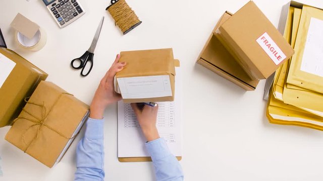 delivery, mail service, people and shipment concept - woman with parcel boxes and clipboard working at post office
