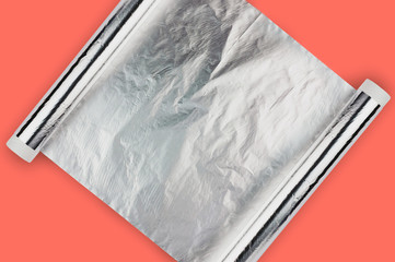 One scroll of glossy aluminium sheet on cardboard tube on table of coral color with copy space for...