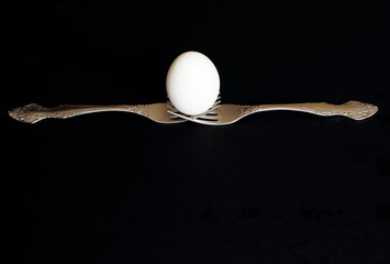 Principle of balance White egg on silver forks on black background. Minimal concept with copy space.