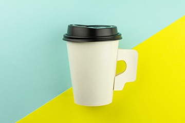 Takeaway paper coffee cup on blue and yellow background.