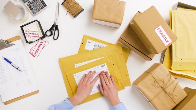 delivery, mail service, people and shipment concept - woman sticking fragile marks to parcel envelopes at post office