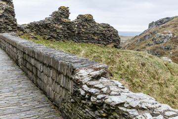 pedestrian walkway made of axial slabs and adjacent low-walled wall; mountain view and historic stone wall fragment