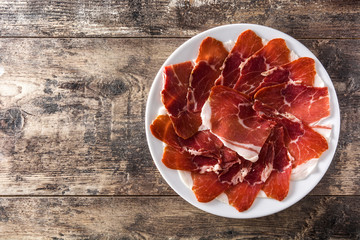 Spanish serrano ham or prosciutto in plate on wooden table on wooden table. Top view. Copyspace