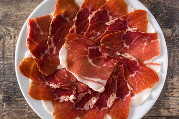 Spanish serrano ham or prosciutto in plate on wooden table on wooden table. Top view