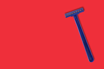 One male disposable plastic razor blue color with two sharp blades on red table in bathroom with copy space for your text. Top view. Hygiene concept