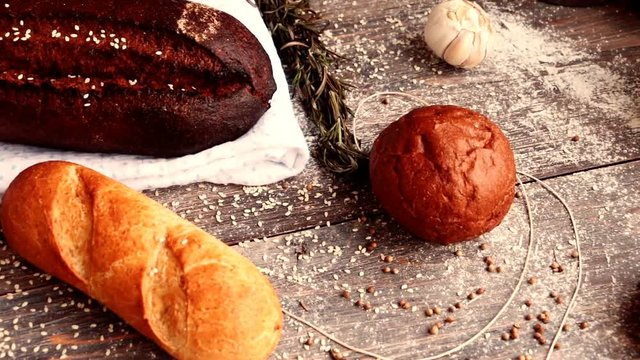 Different types of bread on wooden table dusted with flour. Slow pan.	Concept of natural food and organic food.