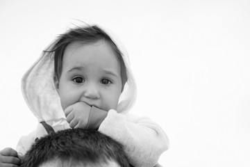 Close up of small baby girl in hood sitting on father's shoulders on the sky background