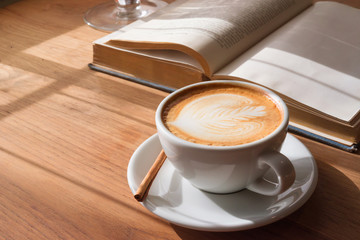 A Cup of hot latte art coffee on wooden table with book in coffee shop cafe.