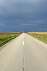 Empty road in autumn day between meadows and fields