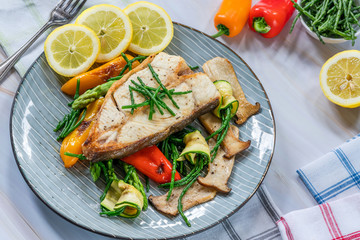 Grilled halibut steak with vegetables - sweet mini peppers, courgette, asparagus and oyster mushrooms, garnished with samphire